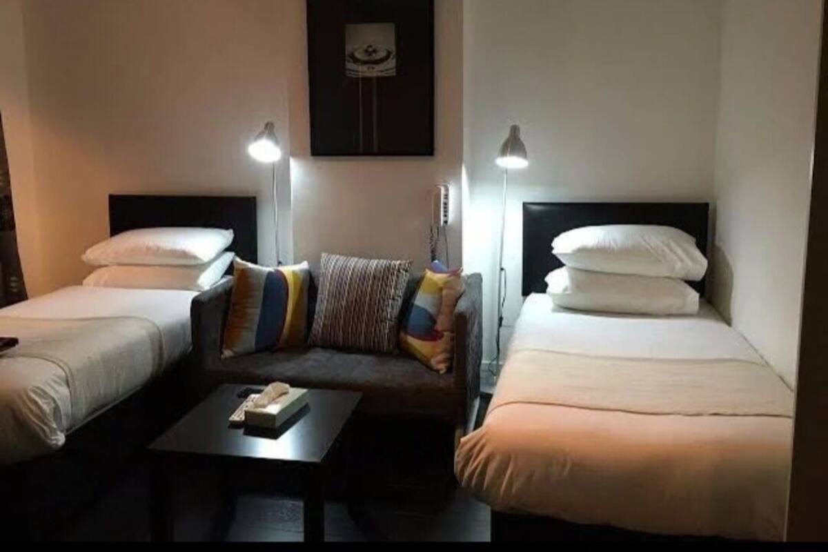 A hotel room with two single beds, a sofa, a coffee table, and two bedside lamps.