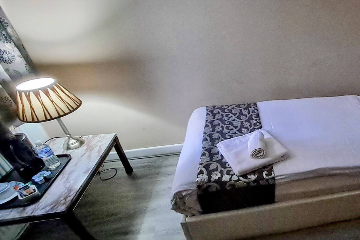A hotel room with a bed, a bedside table with a lamp, and a tray with breakfast items.