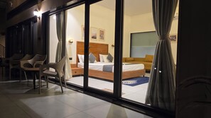 A hotel room with a bed, a sofa, a dining area with chairs, and a view through large glass doors. - Rain Forest Gir Resort (Talala)