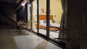 A hotel room with a bed, a nightstand, a chair, and a window with curtains. - Rain Forest Gir Resort (Talala)