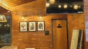 A brick wall with three framed pictures, a wooden door labeled "KITCHEN", and a hanging light fixture. - Rain Forest Gir Resort (Talala)