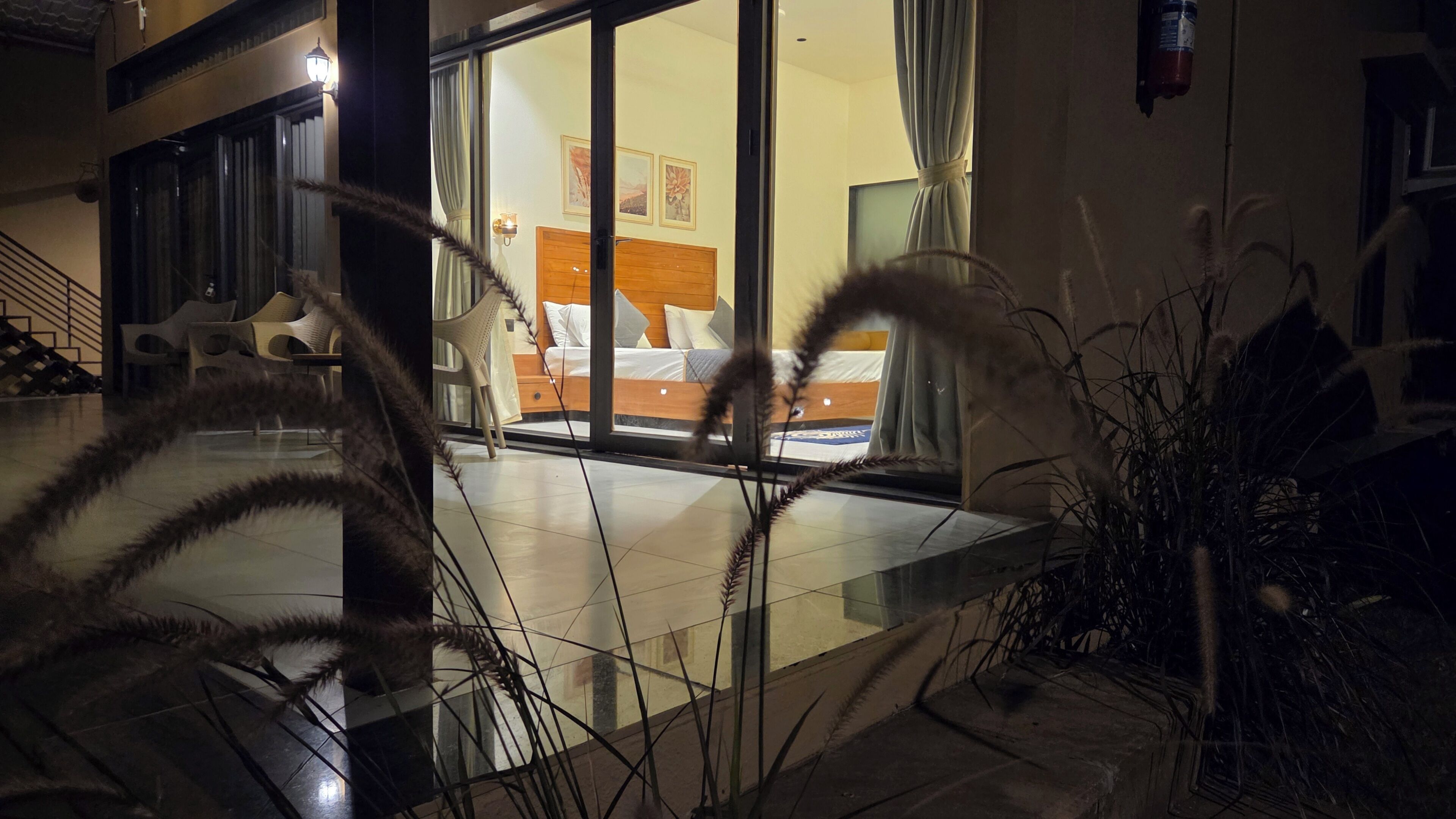 Habitación de hotel con cama, mesita de noche, ventana con cortinas y vistas al exterior.
