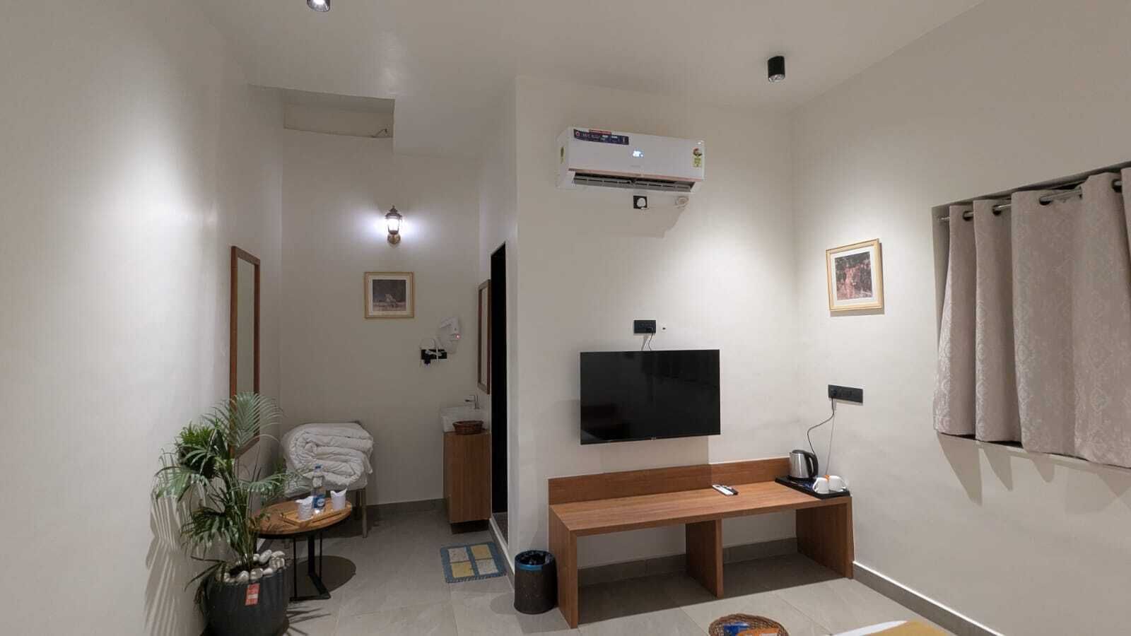 Een compacte hotelkamer met een flatscreen-tv, een houten bankje, een tafeltje met een plant, een handdoekhouder en een douchegordijn.