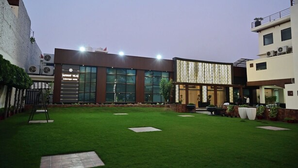 A modern building with large windows, a well-maintained lawn, and outdoor seating. - JASWANT VILAS A BOUTIQUE HOTEL (Prayagraj)