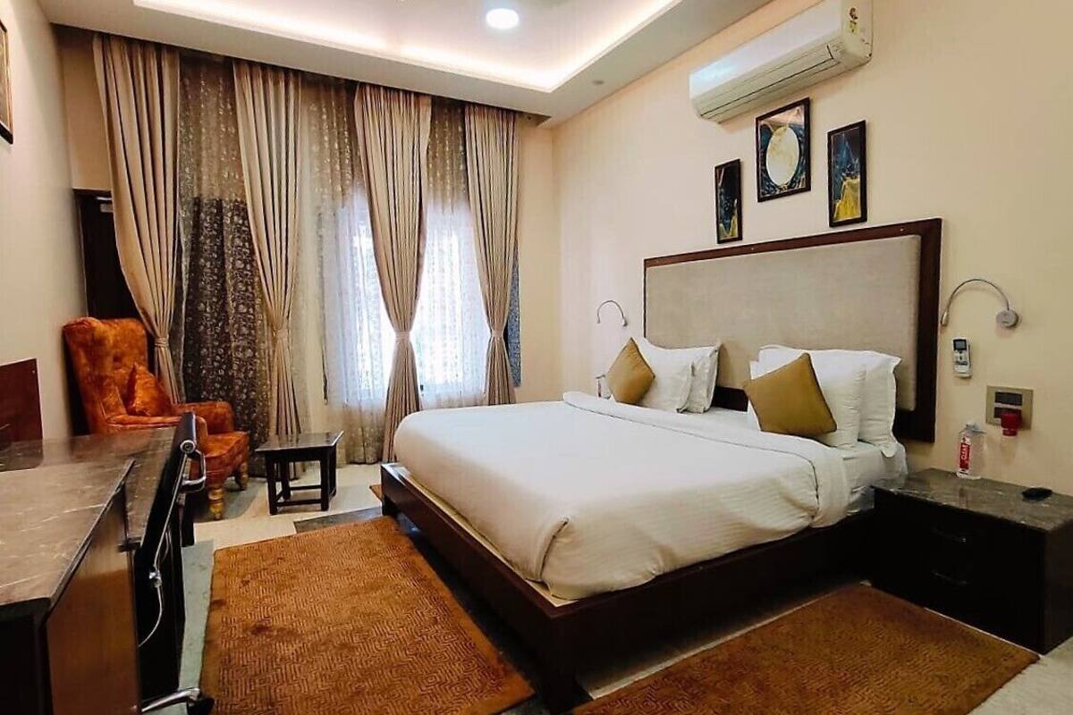 Una habitación de hotel con una cama grande, un escritorio, una silla y un ventanal con cortinas.