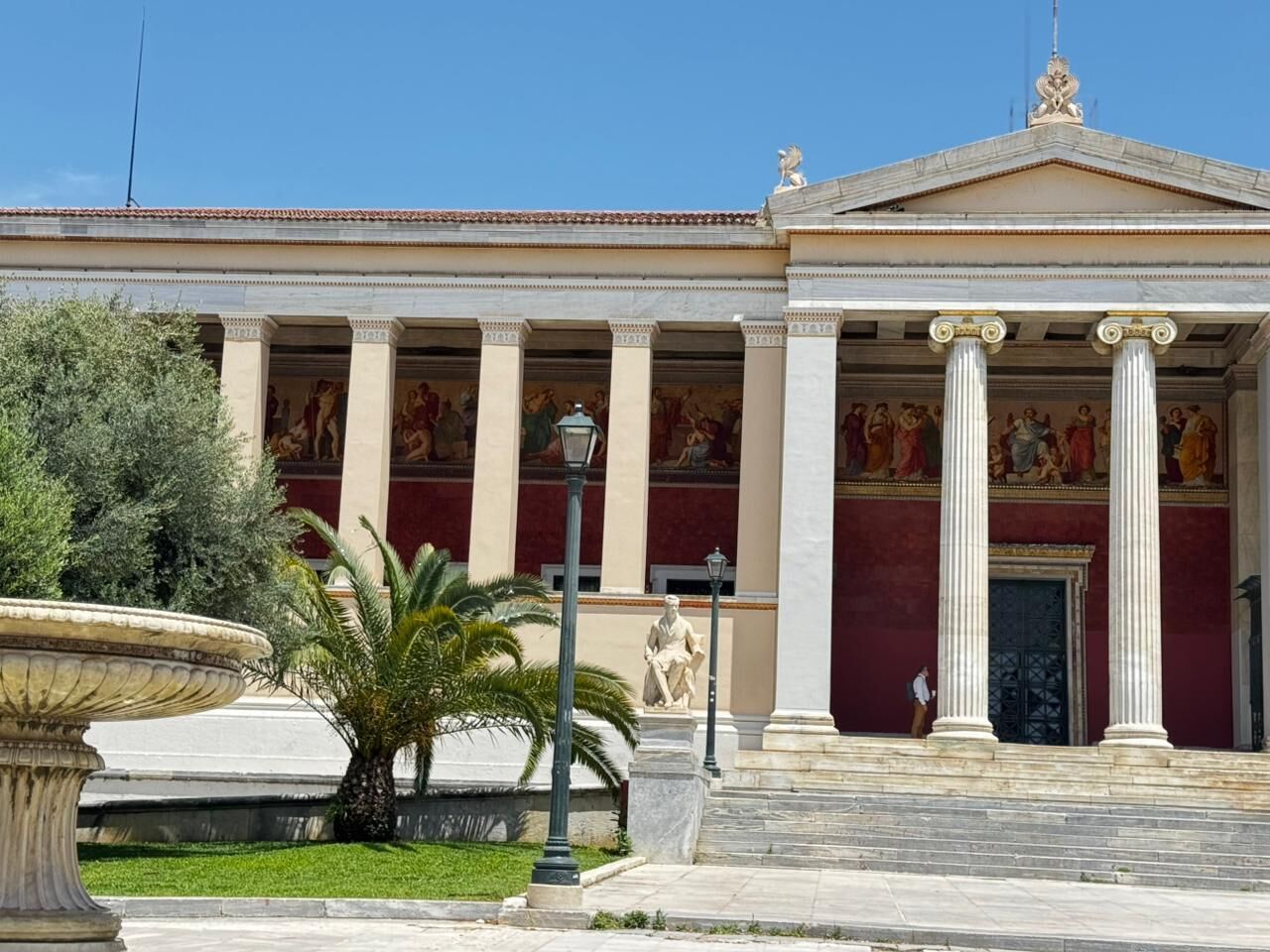 Un bâtiment de style classique, avec des colonnes, une fontaine et une statue à l’avant.
