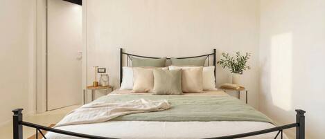 A neatly made bed with a metal frame, a bedside table with a lamp, and a small potted plant.