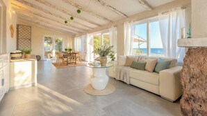 A spacious living area with a glass-top coffee table, a beige sofa, and a view of the sea through large windows. - ClickSardinia Villa Tramonto by the beach with path to the sea (sorso)