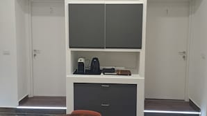 A modern room with a wooden table, two doors, a white cabinet with drawers, and a shelf with electronic devices. - At Home Gaeta Guest House (Rome)