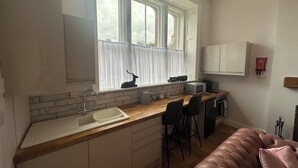 Una cocina con un ventanal grande, un fregadero, un microondas y un taburete de bar.