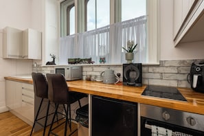 Cozinha moderna com bancada de madeira, forno embutido, máquina de café e janela com cortinas leves.