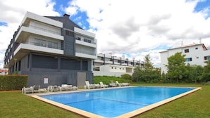Ein modernes Apartmenthaus mit Schwimmbad, Liegestühlen und einem gepflegten Rasen.