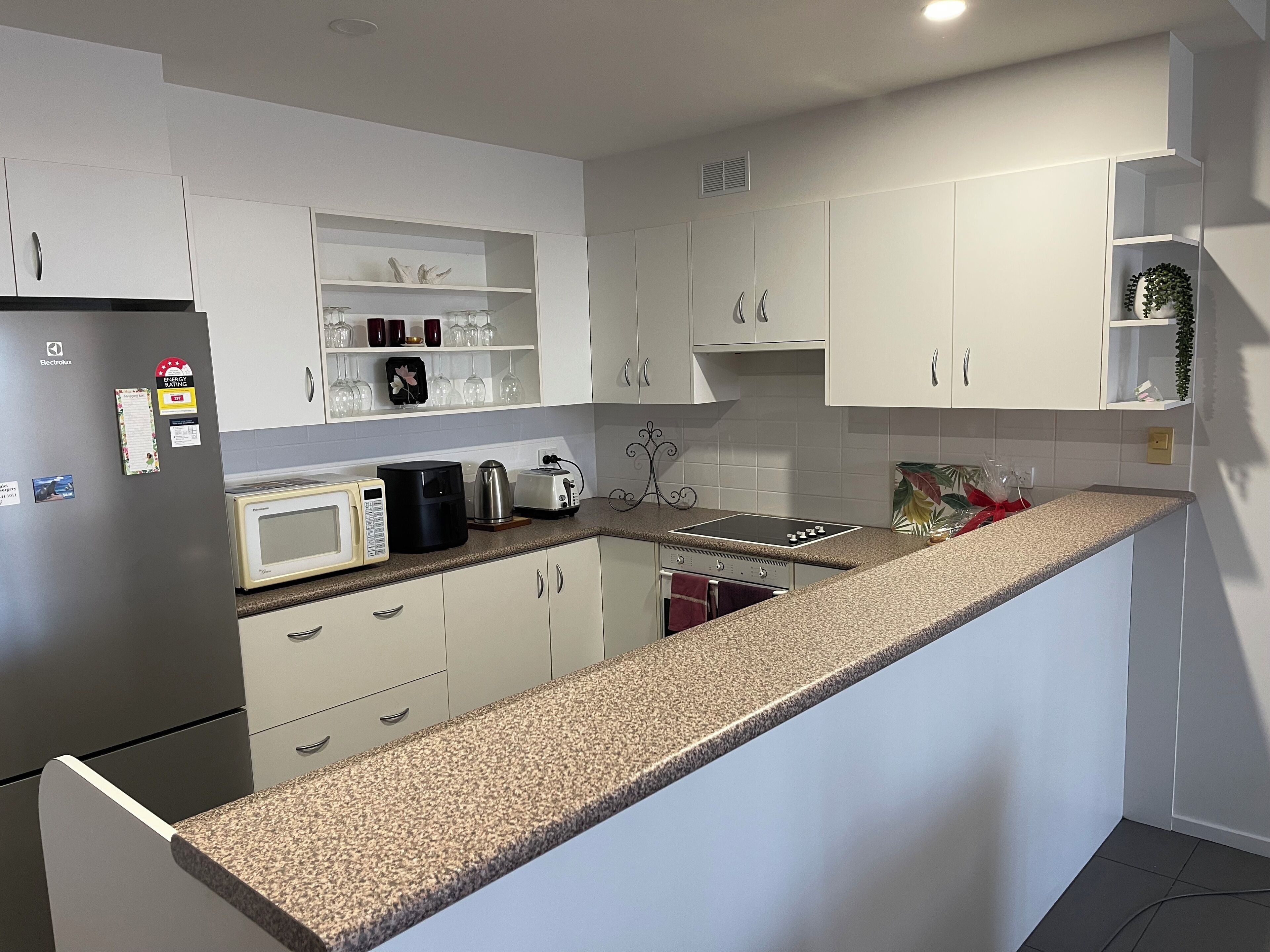 A modern kitchen with white cabinets, a granite countertop, and various appliances including a refrigerator, microwave, coffee maker, and toaster.