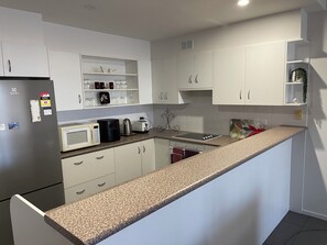 A modern kitchen with white cabinets, a granite countertop, and various appliances including a refrigerator, microwave, coffee maker, and toaster.