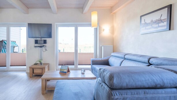 A modern living room with a large grey sofa, a wooden coffee table, and a flat-screen TV mounted on the wall.