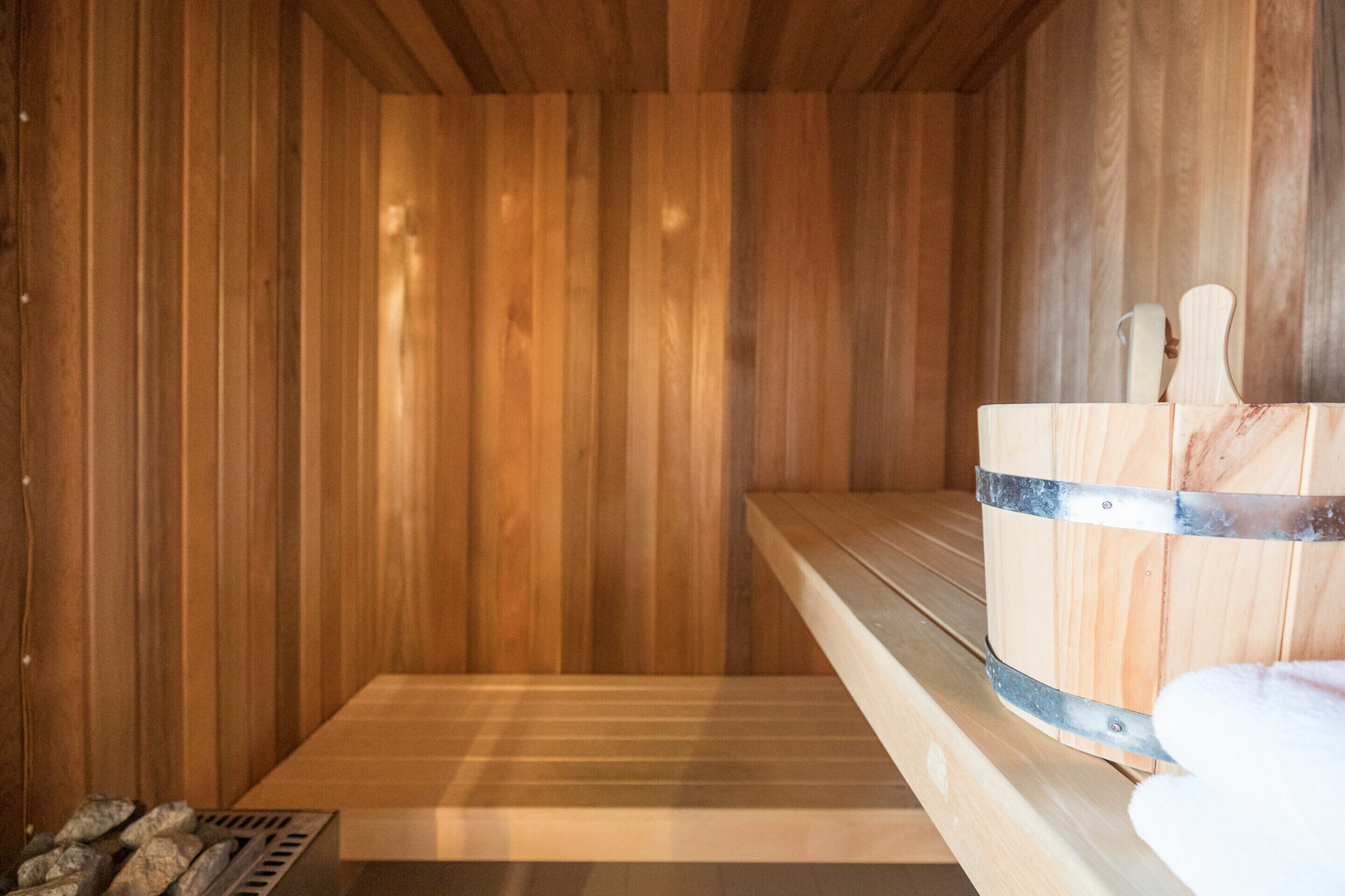 Una sauna de madera con un banco, un cubo de madera y una toalla.