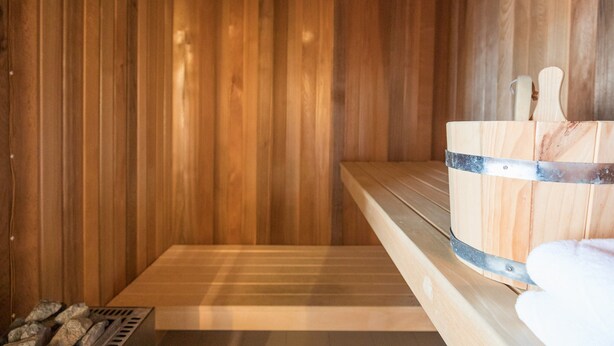 A wooden sauna with a bench, a wooden bucket, and a towel. - Holiday Home in Dagebull With Terrace (Dagebuell)