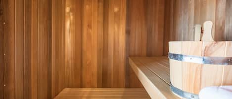 Una sauna de madera con un banco, un cubo de madera y una toalla.
