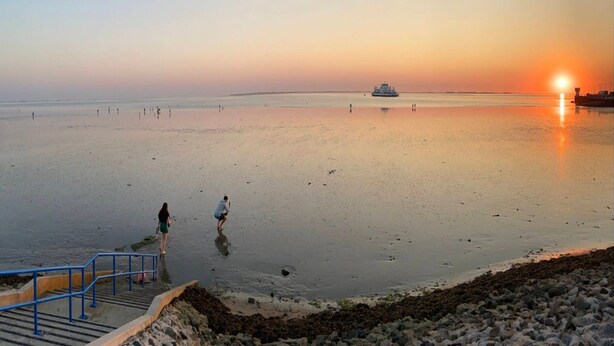 A beach with a sunset, a boat in the distance, and people walking. - Holiday Home in Dagebull With Terrace (Dagebuell)