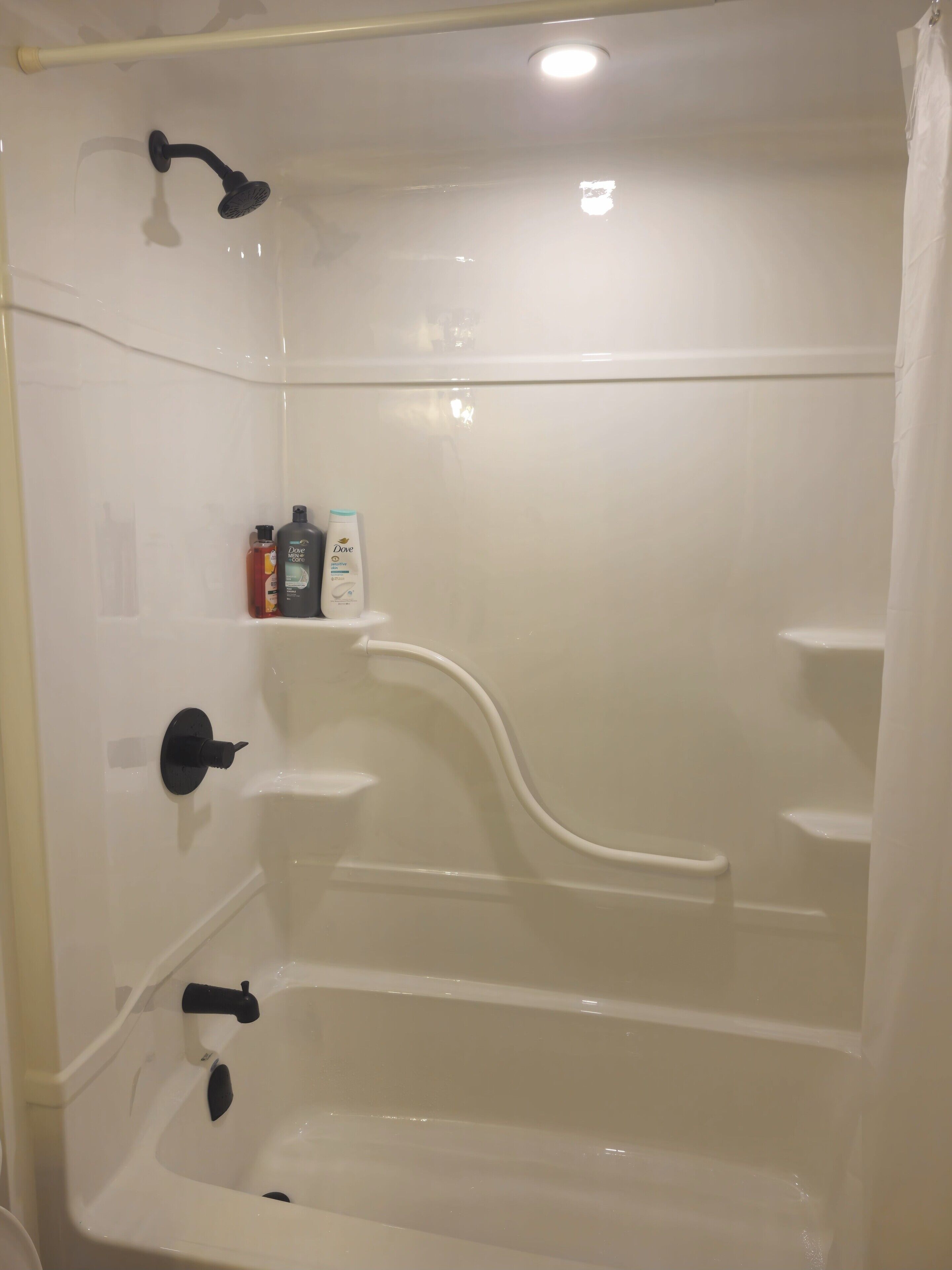 Een wit bad met een handdouche, een ingebouwd plankje met toiletartikelen en een wandmengkraan.