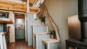 A cozy kitchen with wooden cabinets, a built-in stove, and a window overlooking the interior. - Rowan (Amlwch)