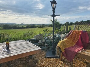 A wooden table with a bottle and glasses, a stone lantern, and a statue of a cat. - Rowan (Amlwch)