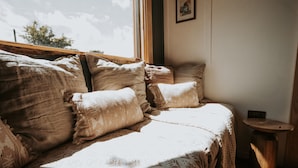 A cozy room with a large bed, a small wooden side table, and a window providing natural light. - Rowan (Amlwch)