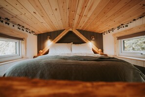 A bedroom with a sloped ceiling, wooden walls, and a bed with white bedding. - Rowan (Amlwch)