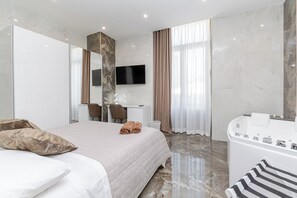Una habitación de hotel moderna con una cama grande, un escritorio, un televisor y un baño con bañera.