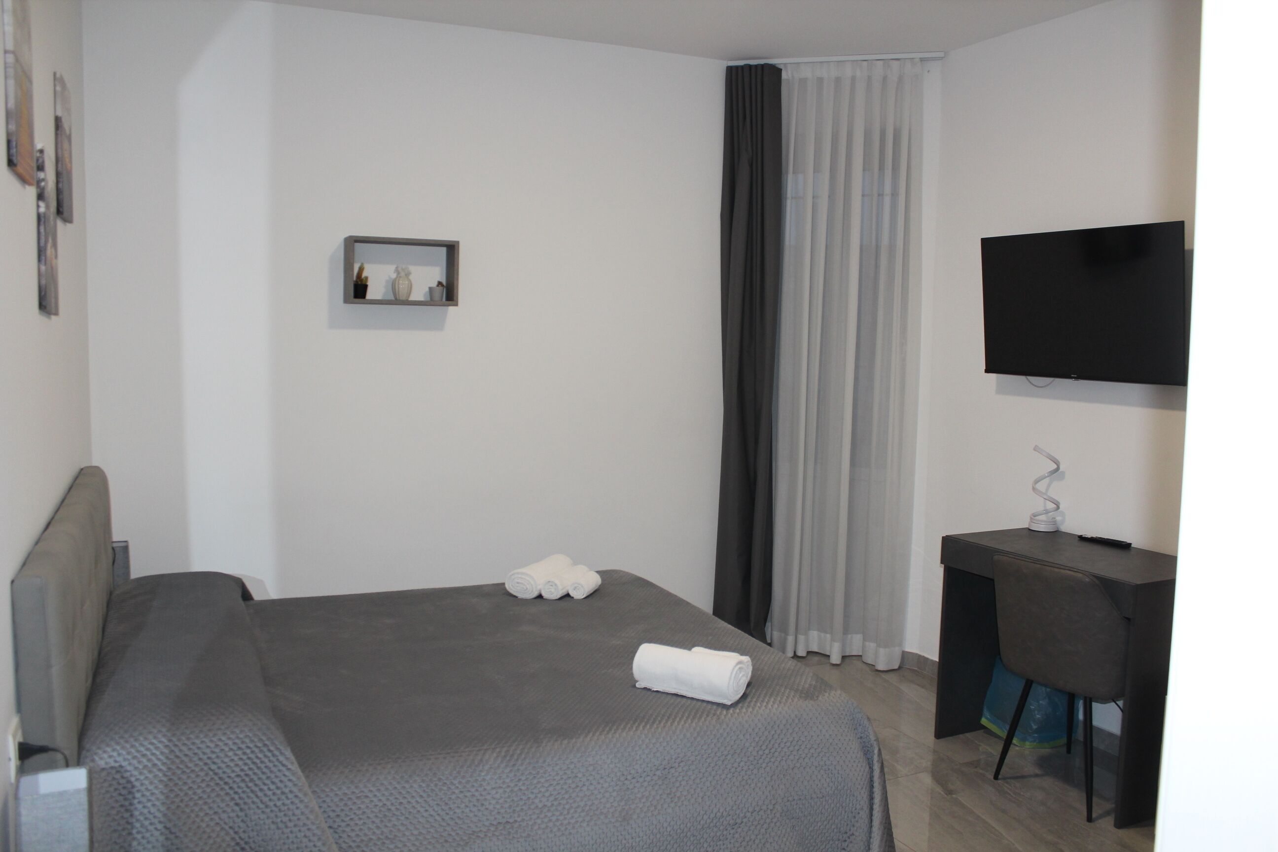 A hotel room with a bed, a desk, a television, and a window with curtains.