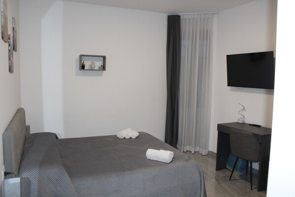 A hotel room with a bed, a desk, a television, and a window with curtains.