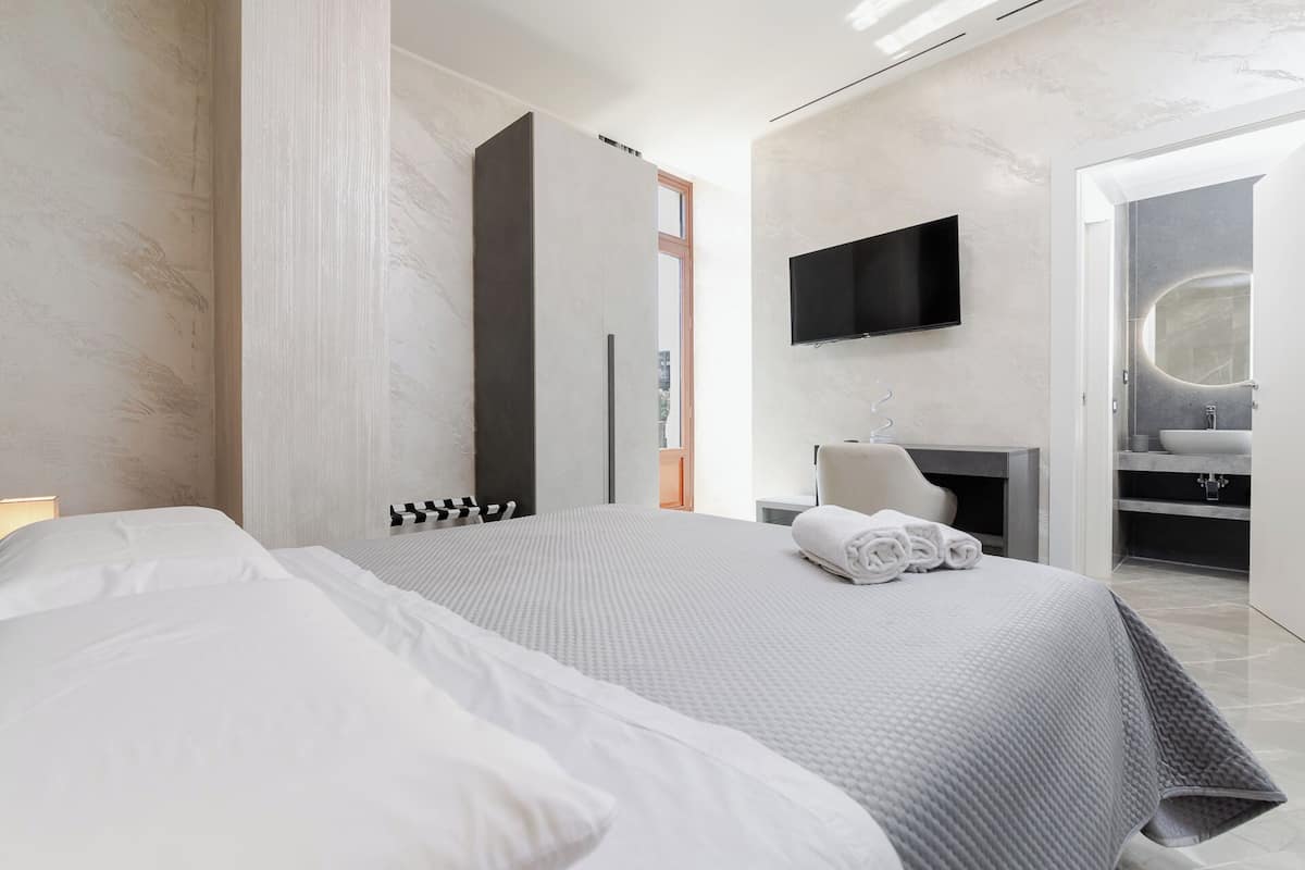 A modern hotel room with a large bed, a flat-screen TV, a bathroom with a vanity, and a large mirror.