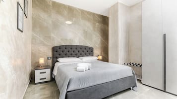 Un dormitorio moderno con una cama de cabecera capitonada, una mesita de noche con lámpara y un armario.