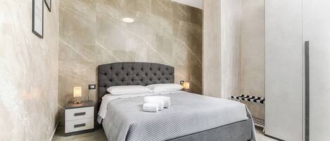Een moderne slaapkamer met een bed met gestuwd hoofdbord, een nachtkastje met een lamp en een kledingkast.