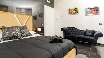 A modern hotel room with a large bed, a black sofa, and two framed pictures on the wall.