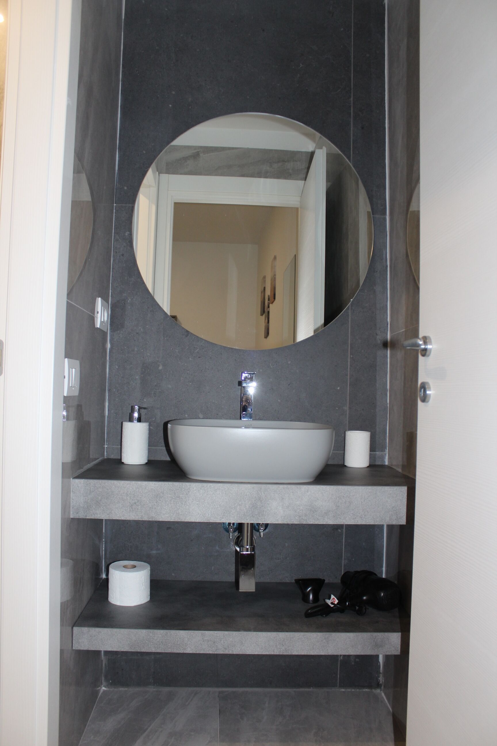 A bathroom with a large oval mirror, a white sink, and a toilet paper holder.