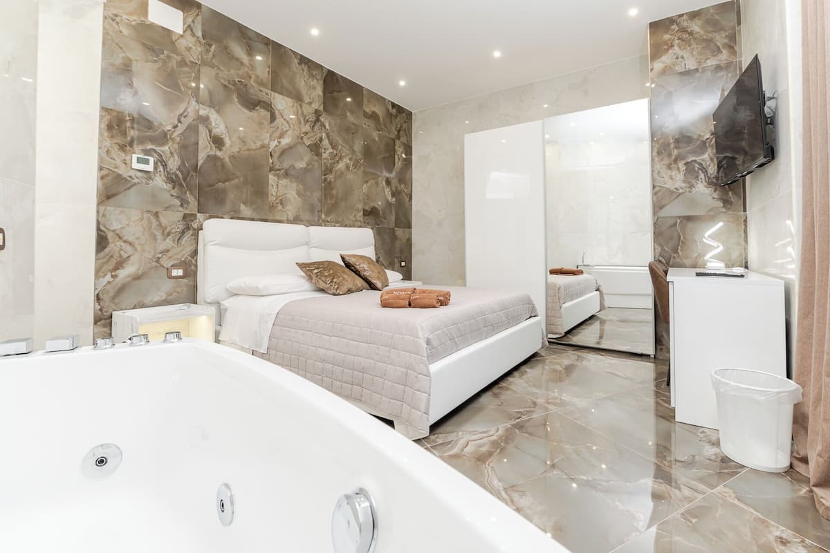 A modern bedroom with a large bed, a separate bathroom, and a flat-screen TV mounted on the wall.