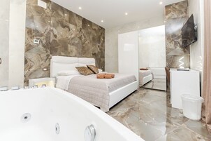 A modern bedroom with a large bed, a separate bathroom, and a TV mounted on the wall.