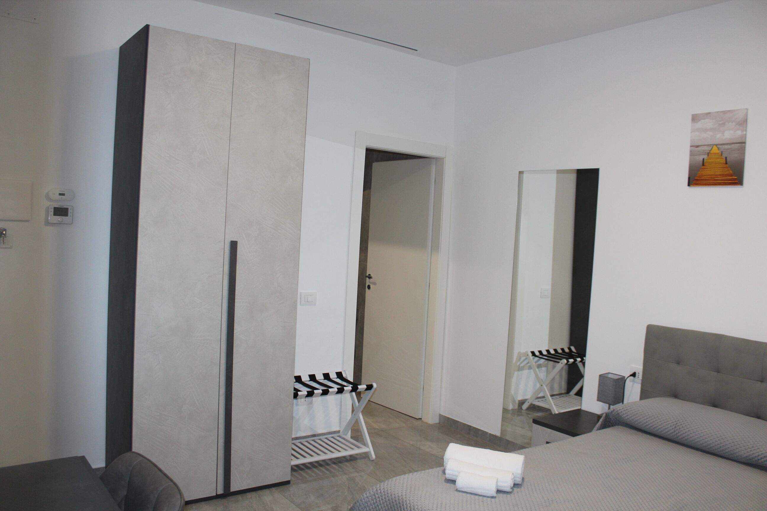 Una habitación de hotel con cama, armario, espejo y un perchero.