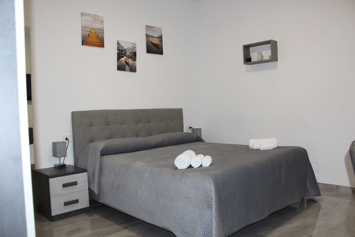 A modern bedroom with a large bed, a bedside table with a lamp, and three framed pictures on the wall.