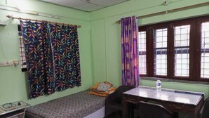 A small, single-bed room with a desk and chair, a window with curtains, and a radiator.