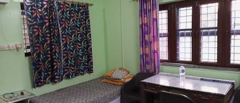 A small, single-bed room with a desk and chair, a window with curtains, and a radiator.