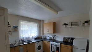 A compact kitchen with a washing machine, stove, refrigerator, and a window with curtains.