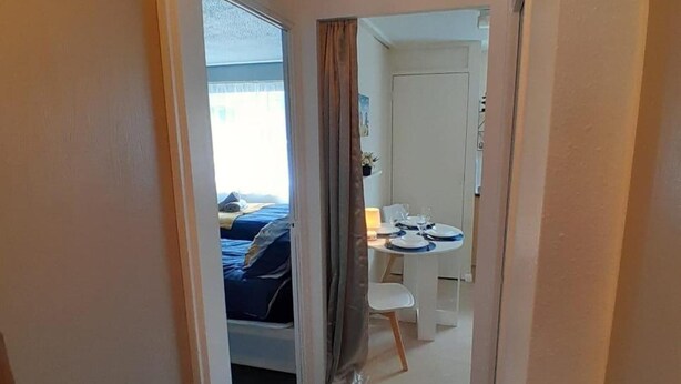 A narrow hallway leading to a bedroom with a bed and a dining area with a table set for two.