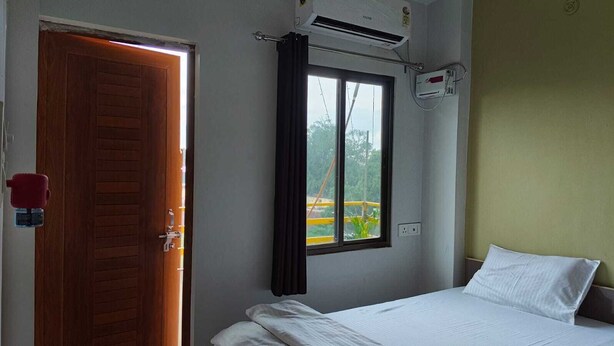Une chambre d’hôtel avec un lit, une fenêtre avec des rideaux, un appareil de climatisation et une porte.