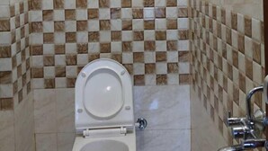 Une petite salle de bain avec des toilettes, une douche et des murs carrelés.