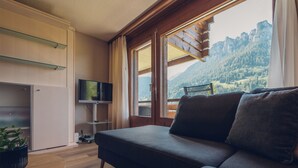 A modern living room with a sofa, TV, and a view of mountains through large windows. - Wirie-Lodge in Diemtigen Holiday apartment on the Wiriehorn - Mountains & relaxation (Diemtigen)