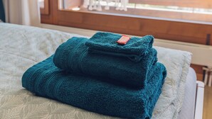 A neatly made bed with folded towels and a view of a balcony with a chair and a plant. - Wirie-Lodge in Diemtigen Holiday apartment on the Wiriehorn - Mountains & relaxation (Diemtigen)