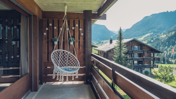 A wooden balcony with a hanging chair, potted plants, and a view of a mountain landscape. - Wirie-Lodge in Diemtigen Holiday apartment on the Wiriehorn - Mountains & relaxation (Diemtigen)
