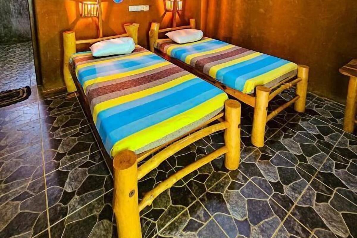 Una habitación con dos camas de madera, un ventilador de techo y mosquiteras.